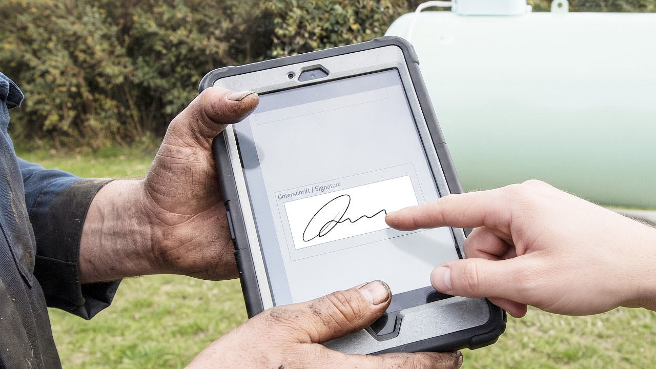 Kunde unterschreibt mit dem Finger auf dem Tablet, das der Monteur ihm hinhält
